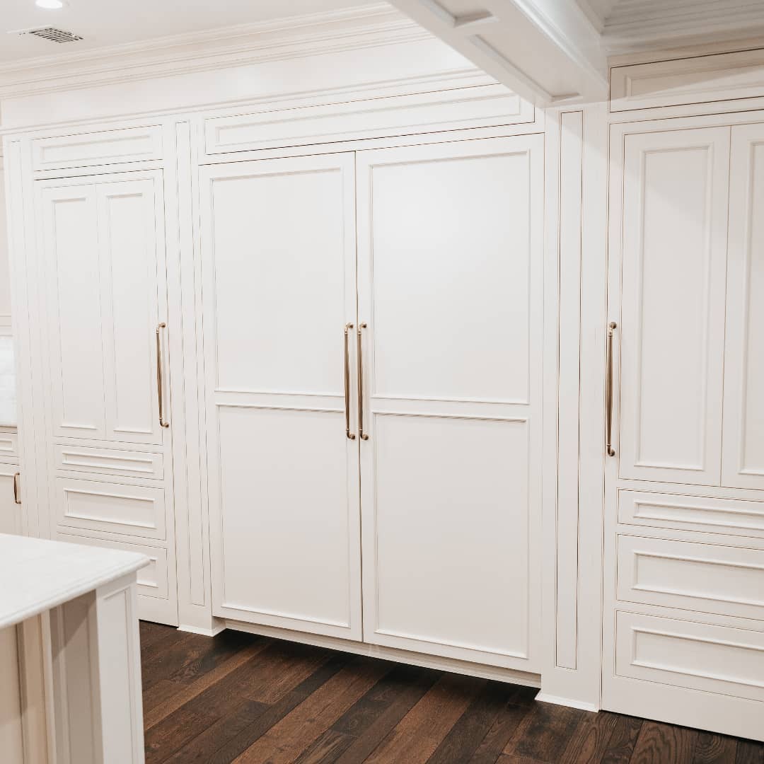 A panel-ready refrigerator with handles, seamlessly integrated into white kitchen cabinetry, enhancing the room’s aesthetic.