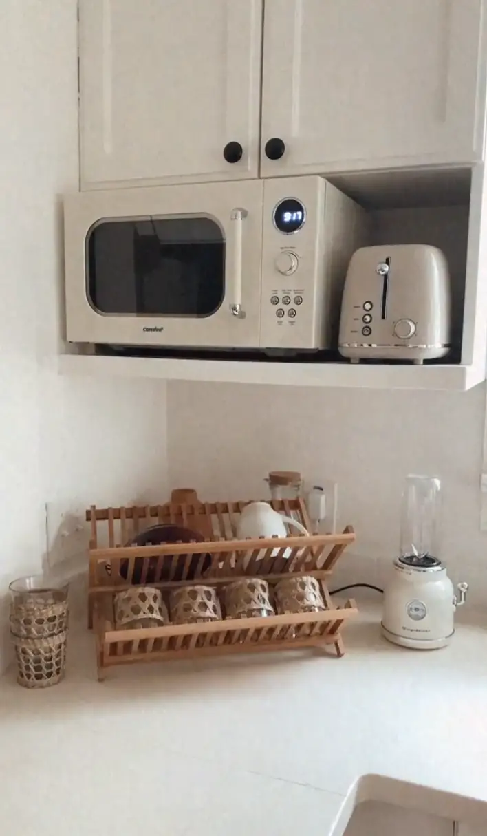 A retro-style microwave and toaster are placed on a shelf, with a dish rack, blender, and glass jar on the countertop below. 