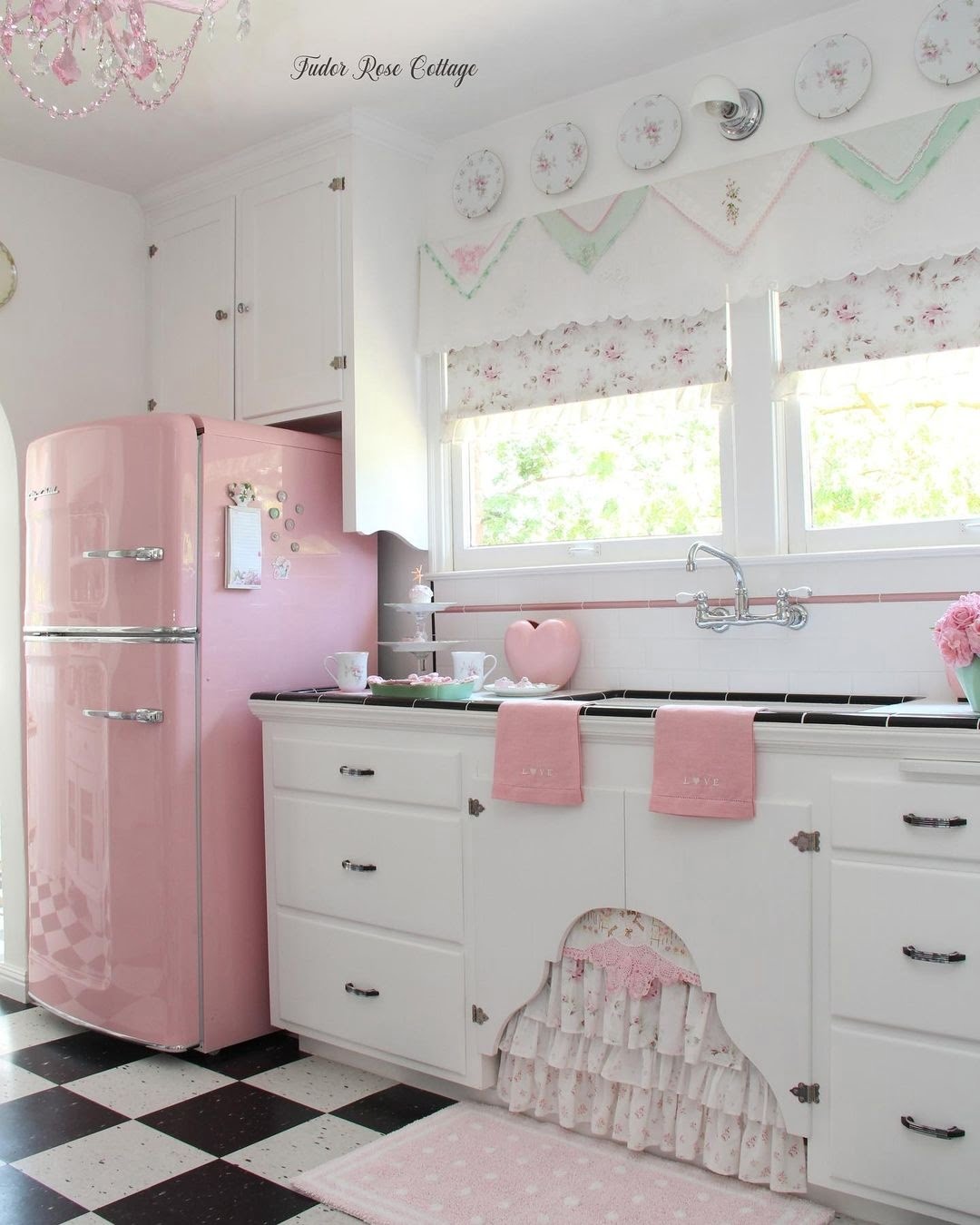 A bright and cozy kitchen interior featuring a retro-style pink refrigerator, white cabinetry, and decorative elements evoking a nostalgic ambiance.