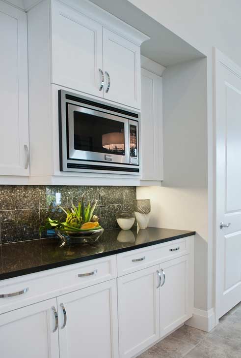 A corner of a modern kitchen with white cabinets, a built-in microwave, dark granite countertop, and decorative items.