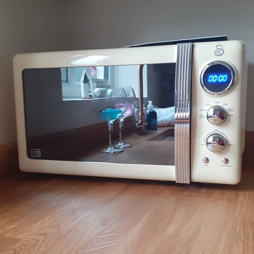 A cream-colored retro style microwave with a digital display and chrome accents, sitting on a wooden floor.