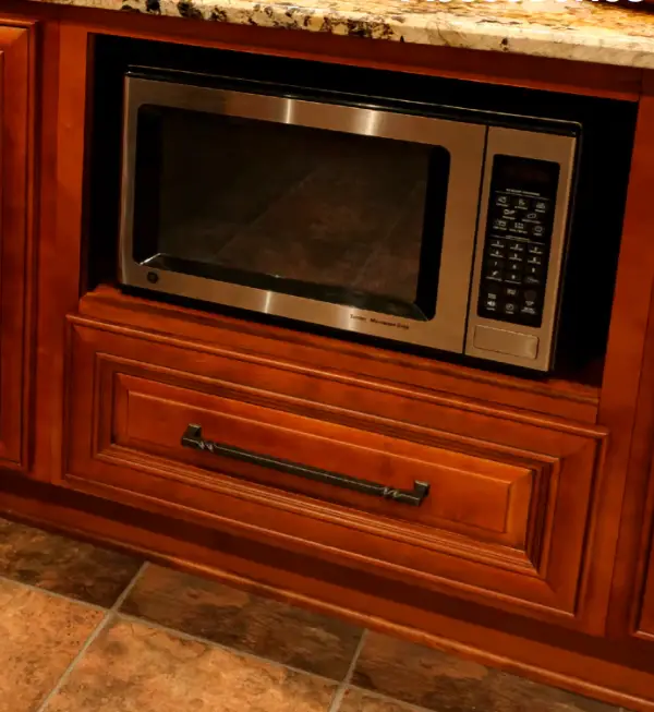 A microwave oven with a digital keypad is built into a polished wooden cabinet beneath a granite countertop.