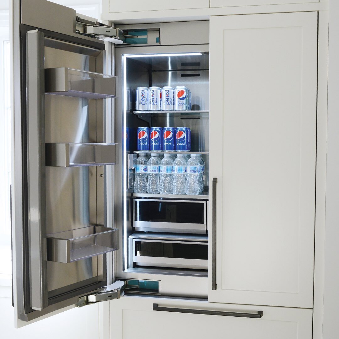 An open panel-ready refrigerator integrated into white cabinetry, stocked with soda cans and water bottles.