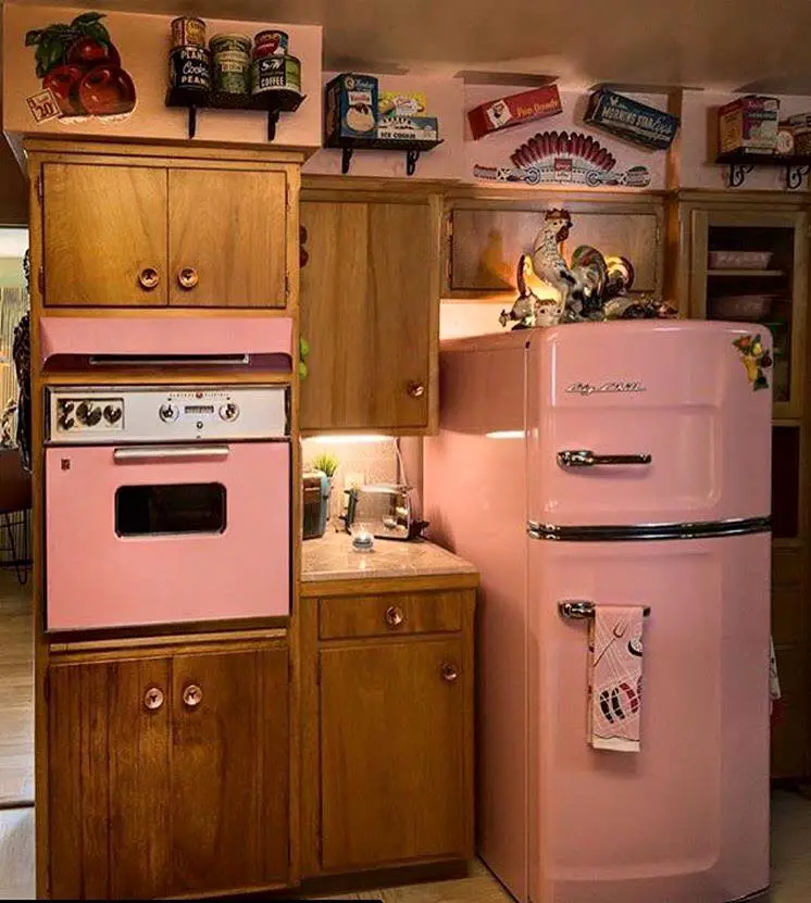 A pink retro refrigerator and oven set in a cozy, vintage-style kitchen.