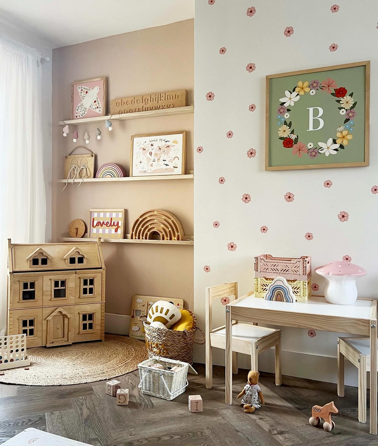 A child’s play corner adorned with a wooden dollhouse, whimsical wall decorations, and a small table set against a backdrop of floral wall art.