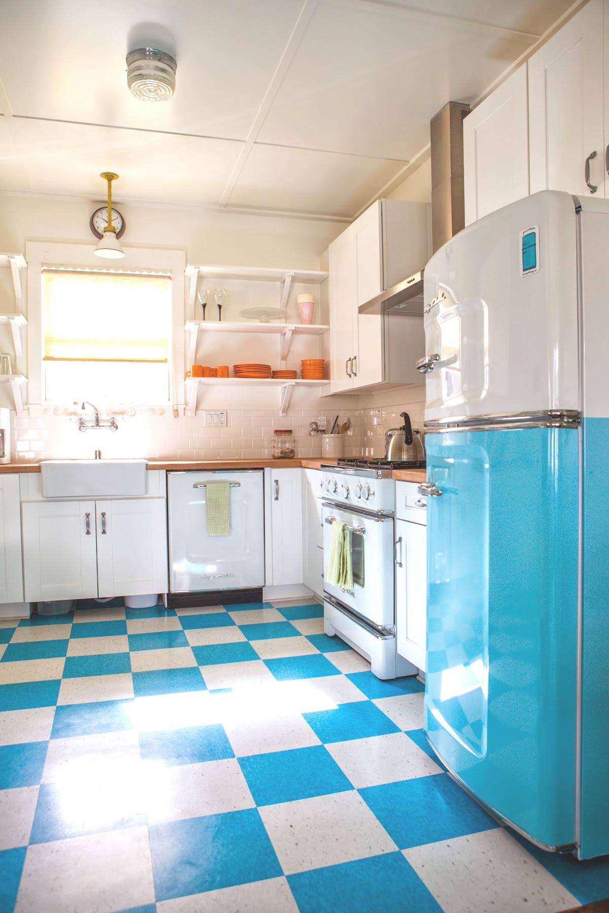 A bright kitchen with white cabinets, a blue and white checkered floor, and a retro-style turquoise refrigerator.