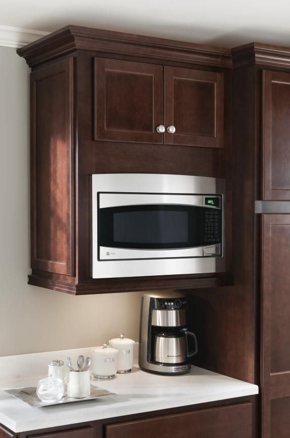 A microwave oven is mounted under a dark wooden cabinet, above a coffee maker that’s placed on a countertop.