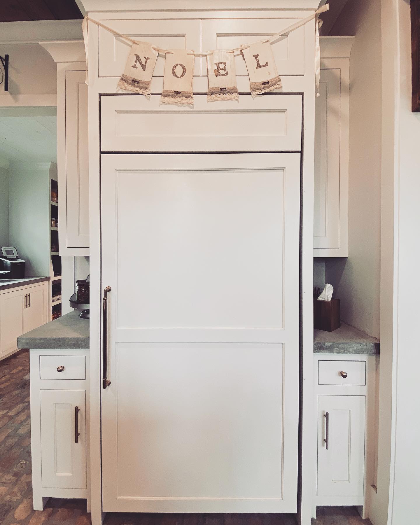 A panel-ready refrigerator seamlessly blending with the white cabinetry in a modern kitchen, adorned with a ‘NOEL’ banner on top.