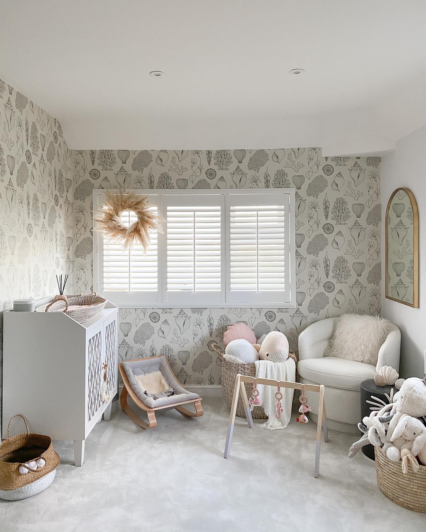 A beautifully decorated nursery with a neutral color palette, featuring a patterned wallpaper, cozy seating, and an assortment of plush toys.