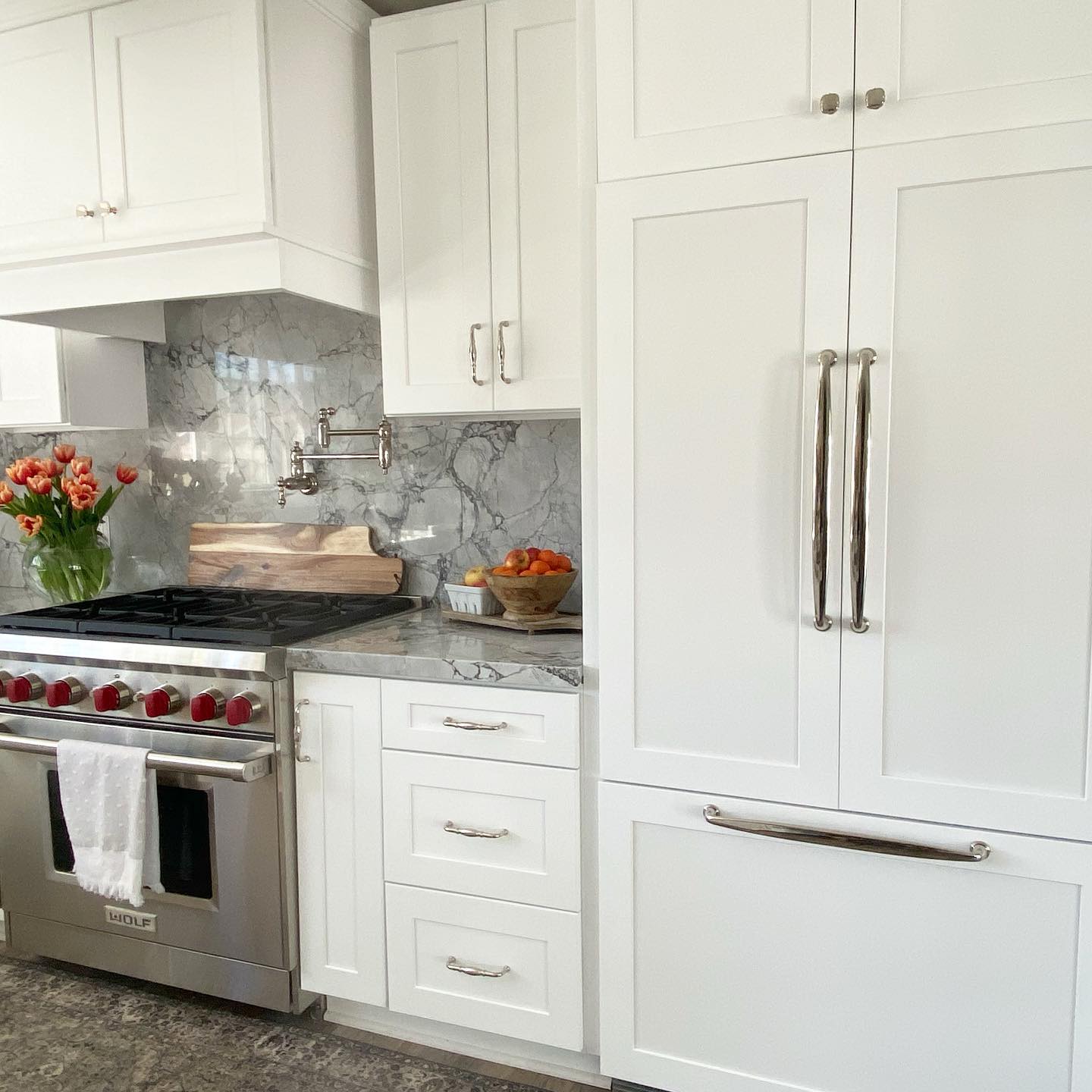 A modern, bright kitchen featuring a panel ready refrigerator that blends seamlessly with the white cabinetry, next to a stainless steel oven and a marble countertop.