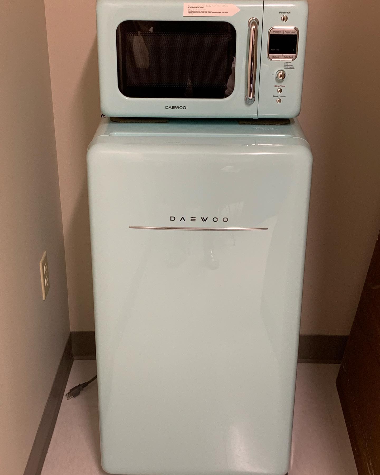 A mint green retro-style Daewoo microwave sits atop a matching refrigerator, both placed in a corner. 