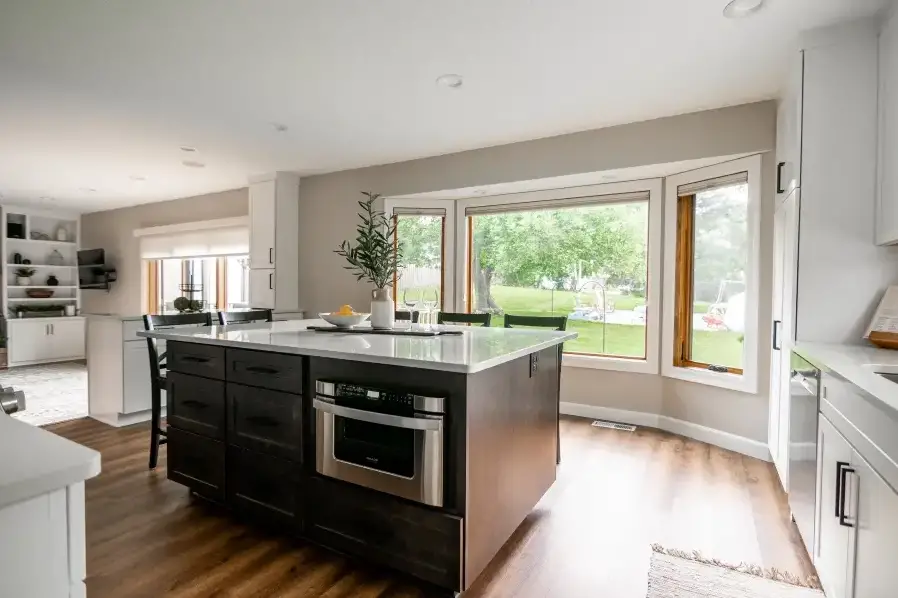 A spacious modern kitchen with a central island, built-in oven, large windows, and a view of the green backyard.