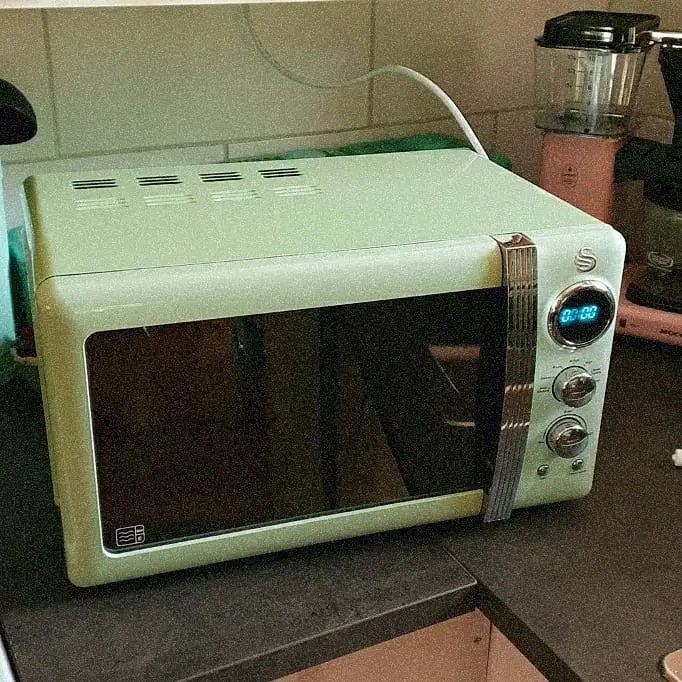 A mint green retro-style microwave with chrome accents, sitting on a kitchen countertop.