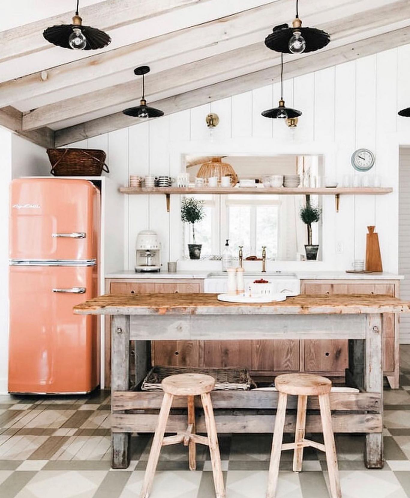 An orange retro refrigerator stands prominently in a well-lit, vintage-styled kitchen with wooden furniture and modern amenities.