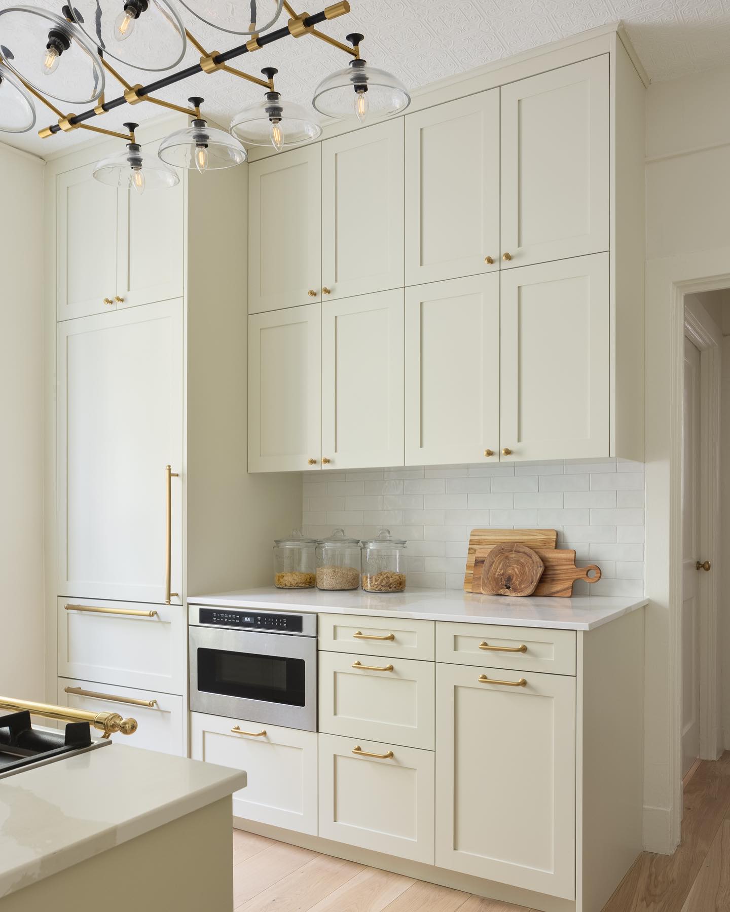 A well-lit modern kitchen featuring a built-in microwave, white cabinets with gold handles, and a stylish chandelier. 